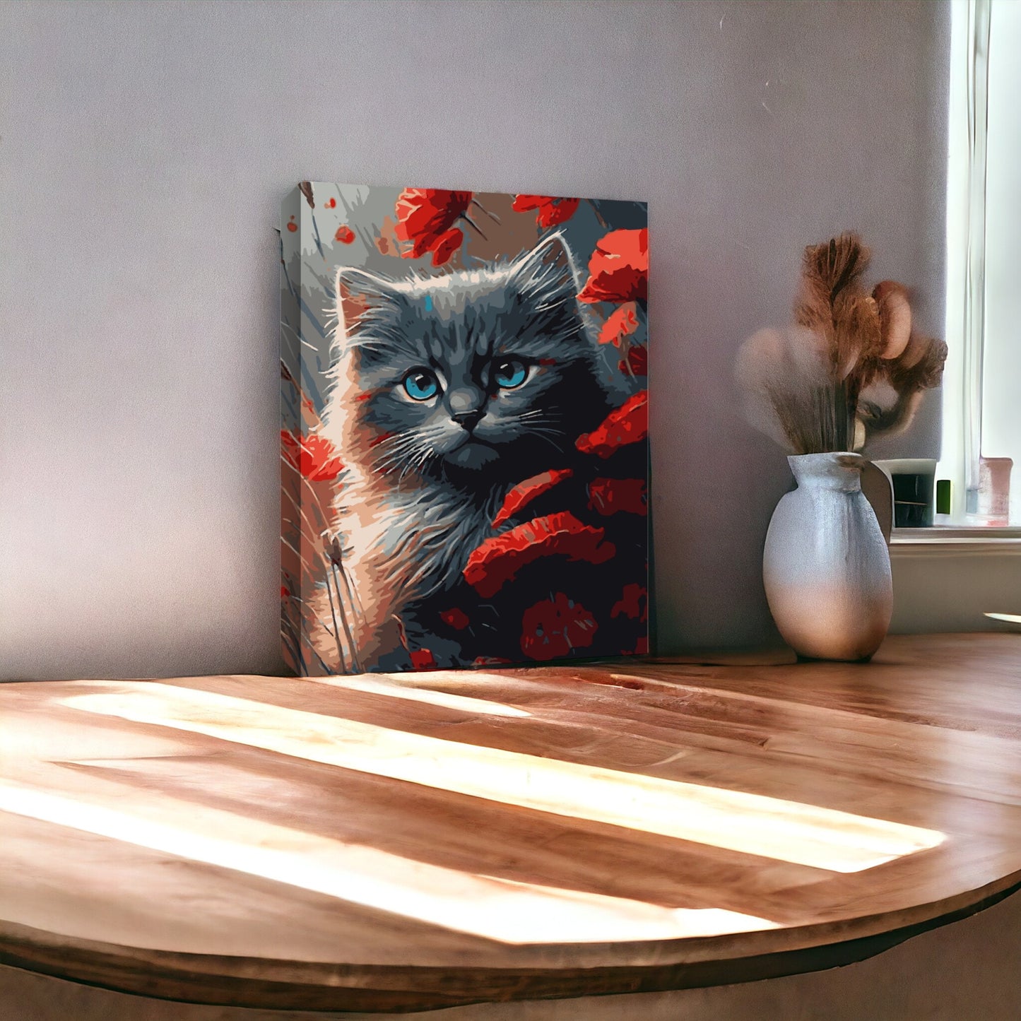 Peinture d'un chat gris entouré de coquelicots rouges posée sur une table en bois, à côté d'un vase contenant des herbes séchées. La lumière naturelle illumine la table, créant des ombres douces dans la pièce.