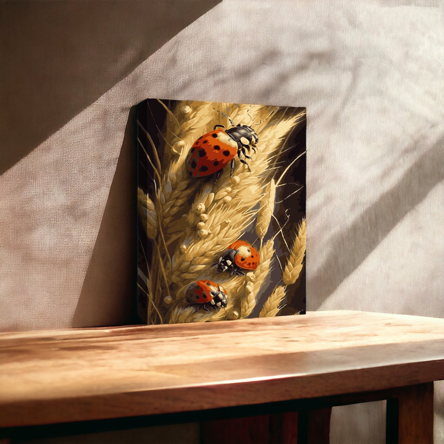 Peinture représentant des coccinelles sur des épis de blé, posée contre un mur dans une pièce éclairée par une lumière naturelle douce. La toile repose sur une surface en bois, créant une atmosphère chaleureuse avec des ombres projetées sur le mur.