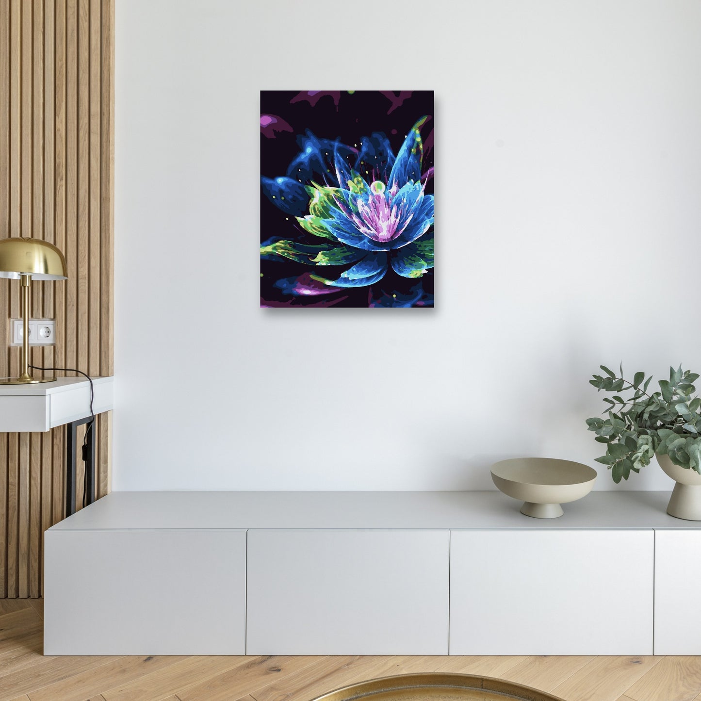 Peinture d’une fleur lumineuse dans des tons de bleu, vert et violet, accrochée sur un mur blanc. La fleur se détache sur un fond sombre, créant un effet éclatant. En dessous, une console moderne est décorée d’objets minimalistes, dont une lampe dorée et un vase avec des branches.