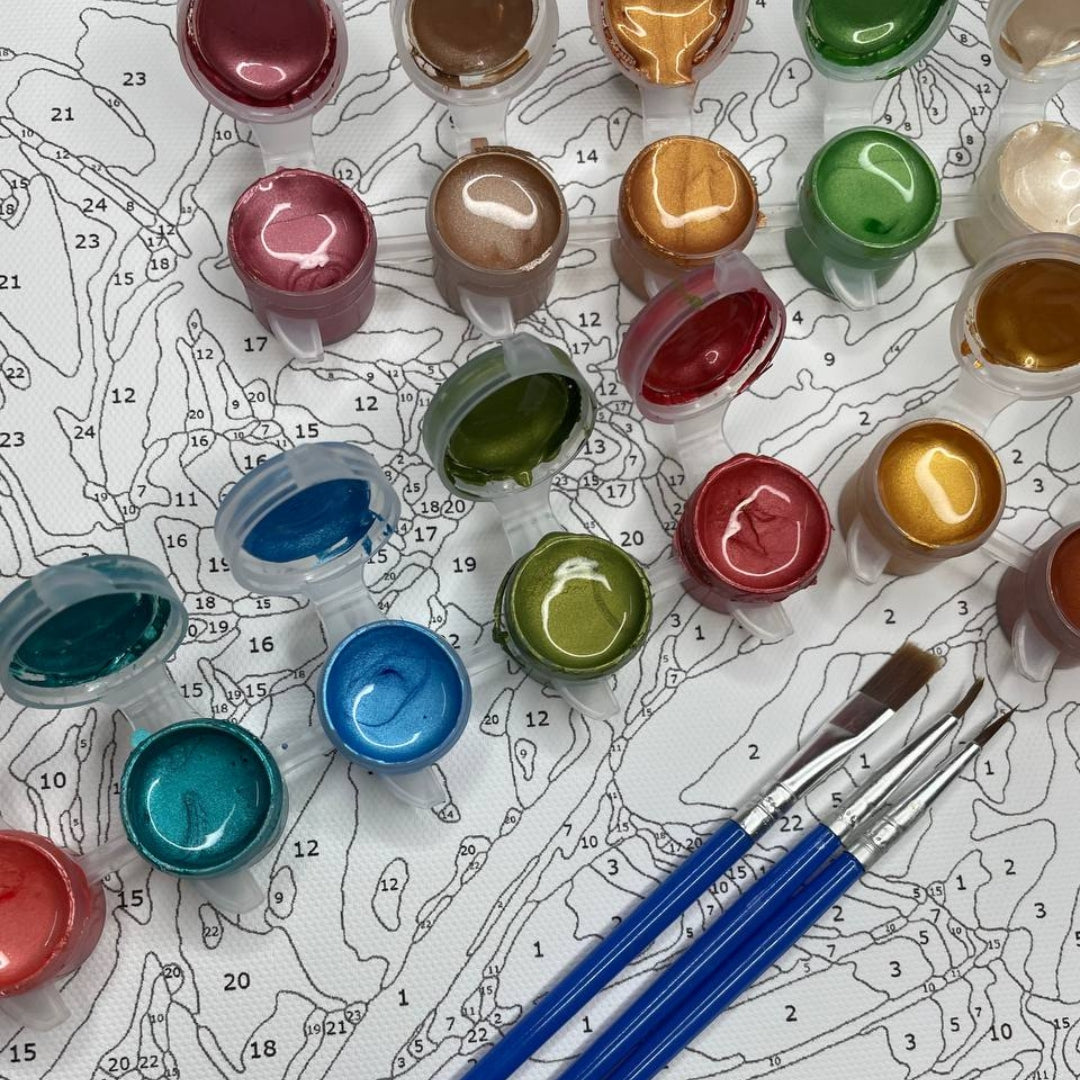 Ensemble de pots de peinture métallisée dans différentes couleurs, avec les couvercles ouverts, disposés sur une toile de peinture par numéros. Trois pinceaux à manche bleu sont posés en bas, prêts à être utilisés pour remplir les zones numérotées sur la toile.