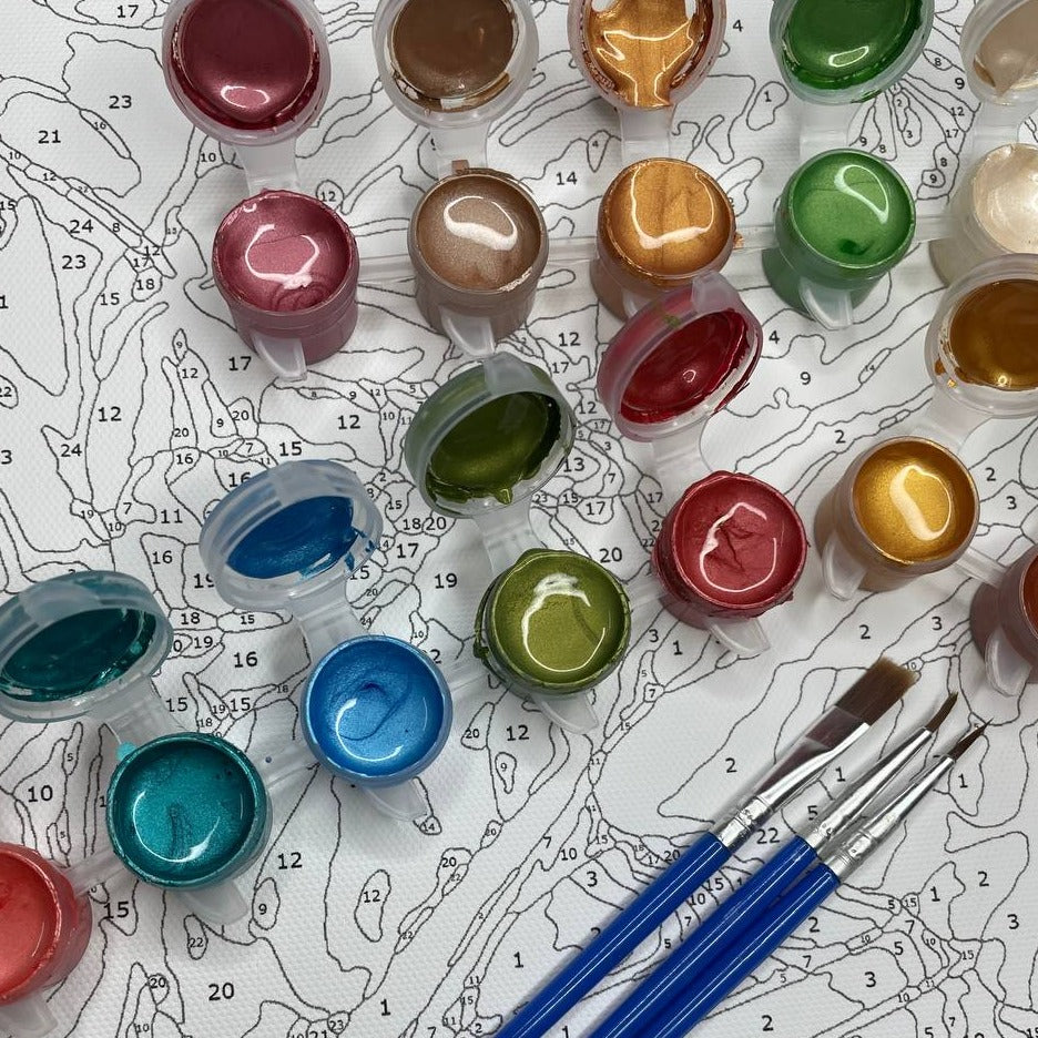 Ensemble de pots de peinture métallisée dans différentes couleurs, avec les couvercles ouverts, disposés sur une toile de peinture par numéros. Trois pinceaux à manche bleu sont posés en bas, prêts à être utilisés pour remplir les zones numérotées sur la toile.