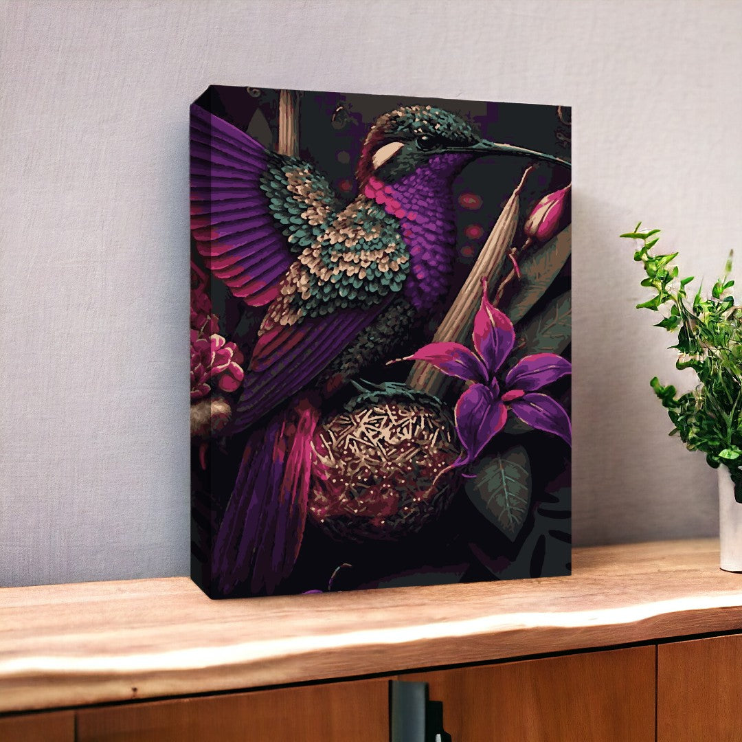 Peinture d’un colibri aux plumes iridescentes violettes et vertes, entouré de fleurs exotiques aux teintes riches, posée sur un meuble en bois clair. Une plante verte en pot est visible à droite, ajoutant une touche naturelle à la scène.