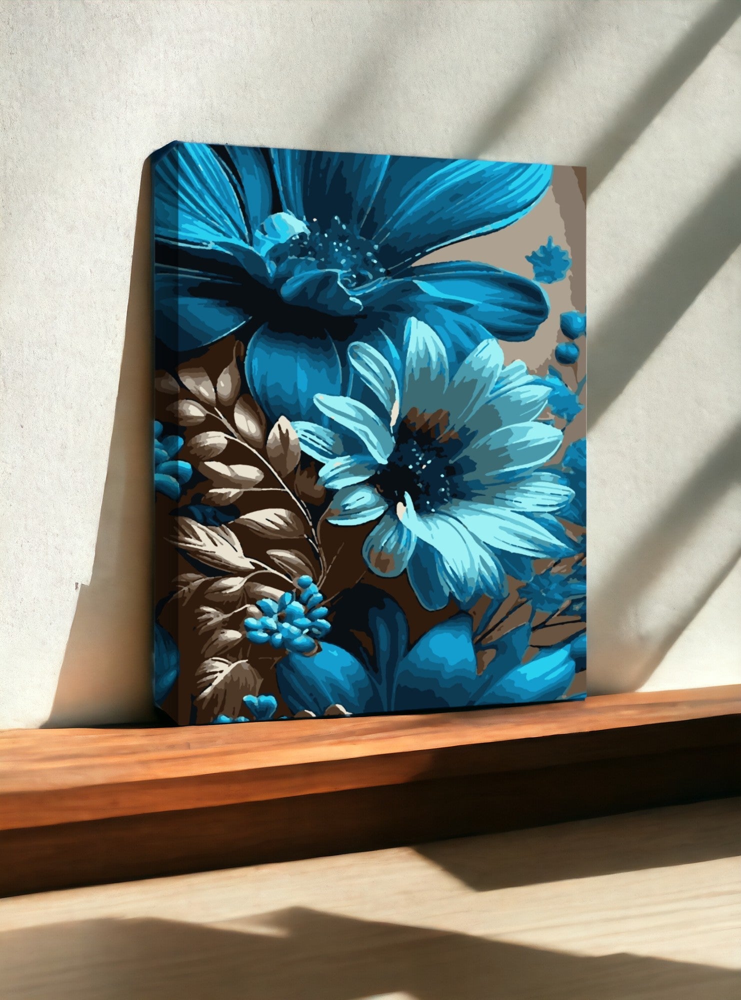 Peinture représentant des fleurs en tons de bleu et brun, posée sur une surface en bois. La lumière naturelle crée des ombres douces sur le mur derrière l'œuvre, mettant en valeur les couleurs vibrantes des pétales.